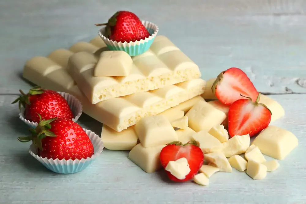 white chocolate bars with squares broken off covered in strawberries on a blue wooden table