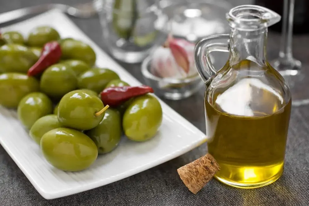 olives on a white plate with a bottle of olive oil on a wooden table