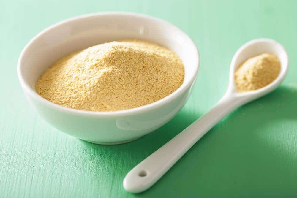 nutritional yeast in a white bowl and spoon on a pale green table