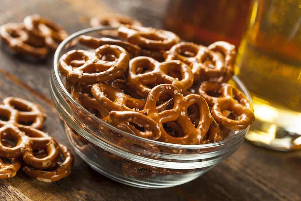 glass bowl full of hard pretzels next to a glass of beer on a wooden table
