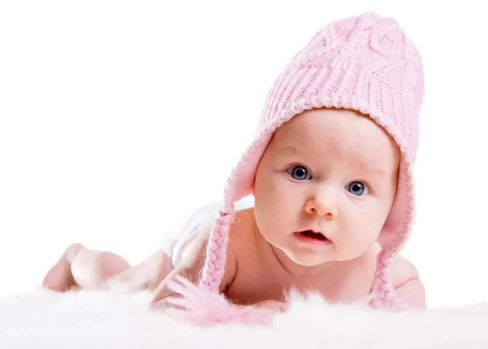 baby in a pink hat laying on a white rug