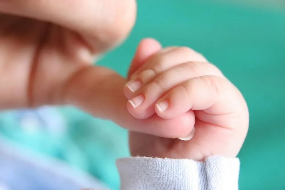 baby holding mom's finger - best postpartum vitamins article